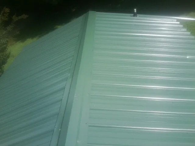New green metal panels meeting at the ridge of a roof — Flat Roof Repair work by our crew in Austin