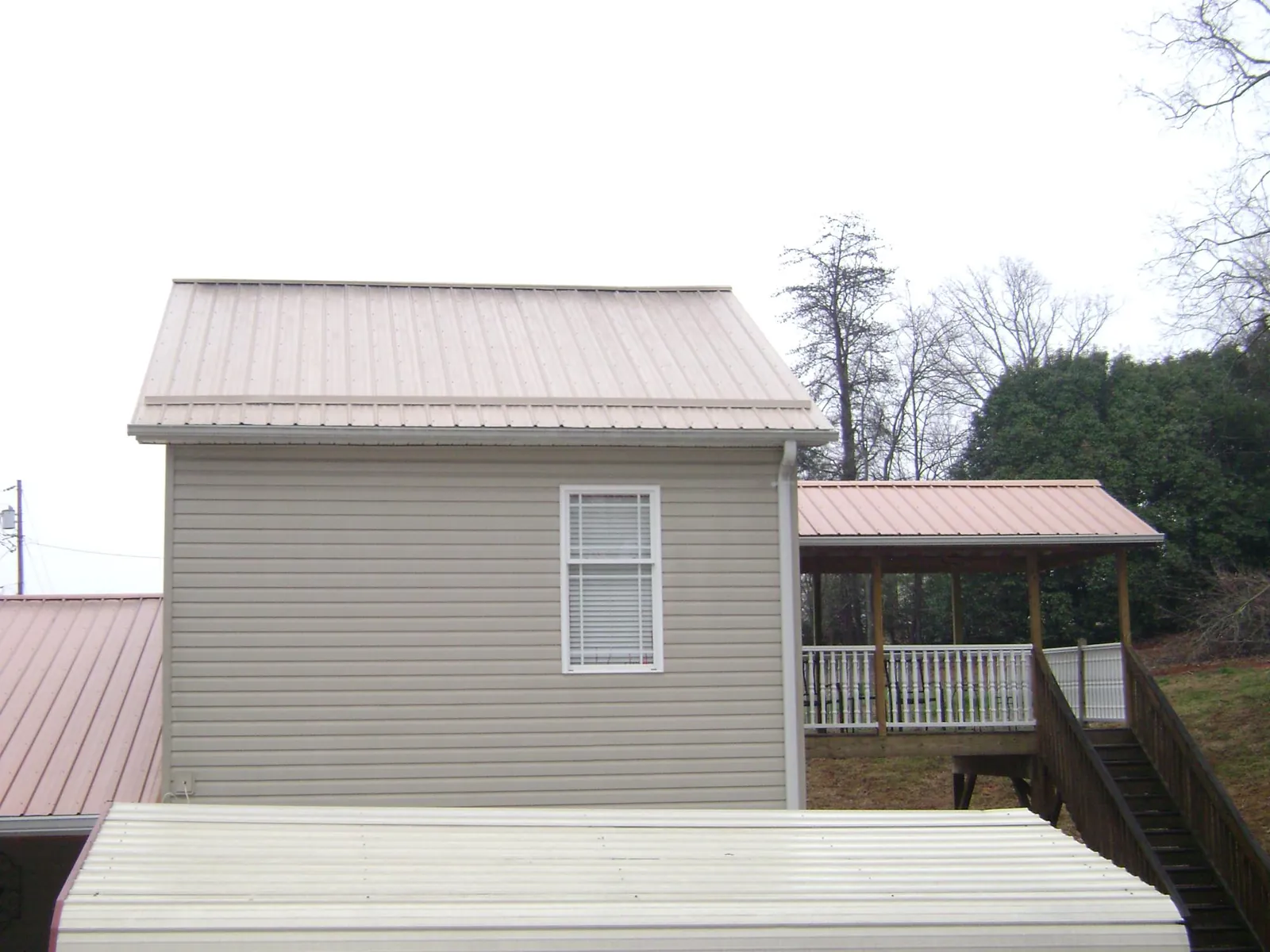 Tan metal roofs on a two story addition and attached porch, from a Roof Replacement job in Austin